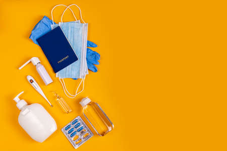 Coronavirus new lifestyle concept. Passports, sanitizer, thermometer, medical gloves, sanitizer gel, blue capsules pill in blister and medical mask on yellow colored background, flat layの写真素材