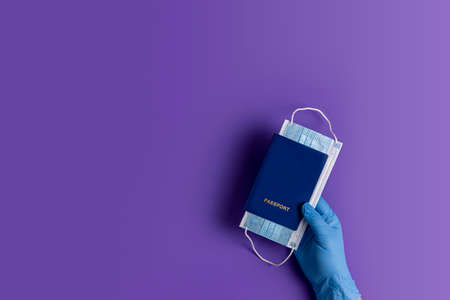 Doctor holds passports and respiratory surgical face mask in hands blue medical glove on violet background. Pandemic corona virus, insurance, airborne diseases, SARS, grippeの写真素材