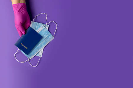 Doctor holds passports and respiratory surgical face mask in hands pink medical glove on violet background. Pandemic corona virus, insurance, airborne diseases, SARS, grippeの写真素材