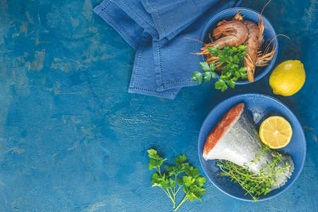 Trout fish surrounded parsley, lemon, shrimp, prawn in ceramic plate. Light classic blue concrete table surface. Healthy seafood background.の写真素材
