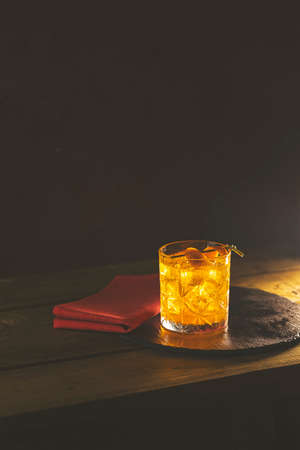 Glass  the cocktail negroni  red napkin and black stone tray on a old wooden board. Drink  gin, martini rosso and orange. Nice romantic backlight.の写真素材