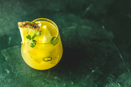 Spicy pineapple jalapeno mezcalita or margarita for Cinco de Mayo is a refreshing cocktail made with pineapple, cilantro, jalapeno and mexican distilled alcoholic beverage on dark green surfaceの写真素材