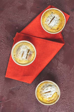 Three apple pies in ceramic baking molds with napkin ramekin on dark red concrete table. Top view, flat lay.の写真素材