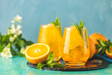 Two glass of orange ice drink with fresh mint on wooden turquoise table surface. Fresh cocktail drinks with ice fruit and herb decoration. Alcoholic non-alcoholic beverage. Mojito on blue backgroundの写真素材