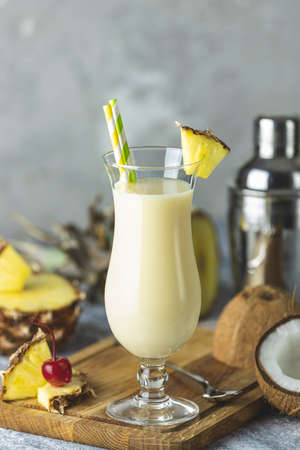 Glass of tasty Frozen Pina Colada Traditional Caribbean cocktail decorated by slice of pineapple, served on light wooden cutting boardの写真素材