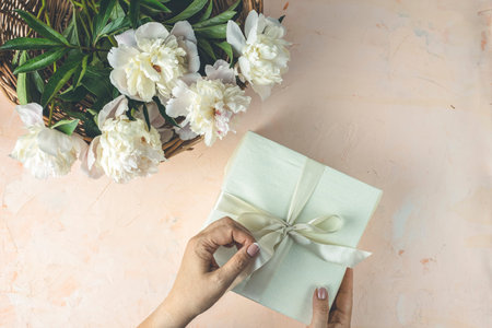 Woman opening her present, top view. Female's hands pull ribbon to unwrap gift box among the white...