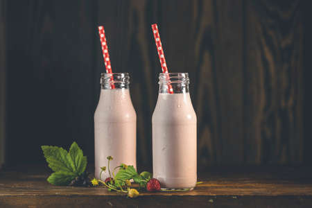 Bottles with delicious strawberry milkshake or smoothie with branch of wild strawberry on dark wooden table and background.の写真素材