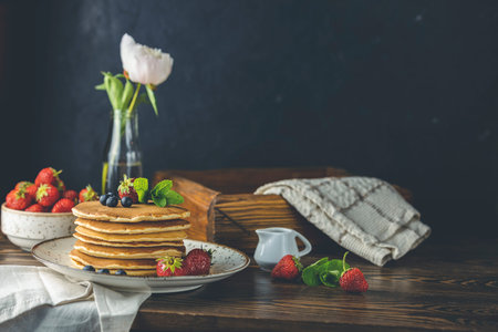 Pancake with srtawberry, blueberry and mint in ceramic dish, syrup from small ceramic jar and...