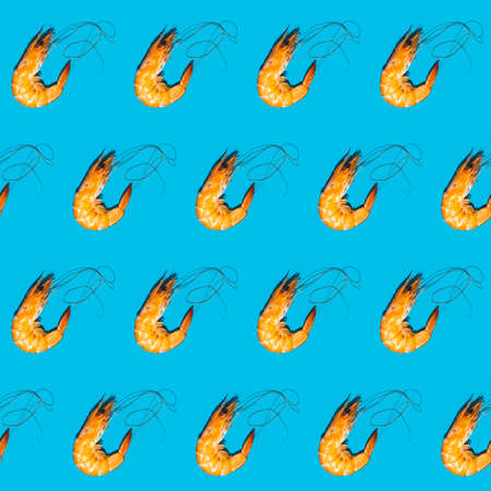 Food diagonal seamless pattern of shrimps on blue background. Creative minimalist flat lay with hard light.の写真素材