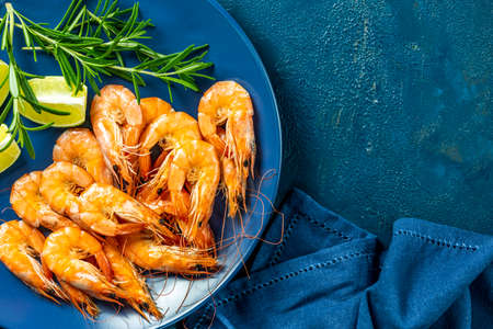 Boiled large shrimp in blue ceramic plate with parsley and lime on dark blue concrete table surface. Fresh seafood ingredient - shrimp tails ready for cooking. Top view, flat lay.の写真素材