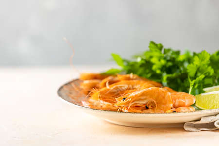 Beautiful boiled large shrimp in light ceramic plate with parsley and lime on pink concrete table surface. Fresh seafood ingredient - shrimp tails ready for cooking.の写真素材