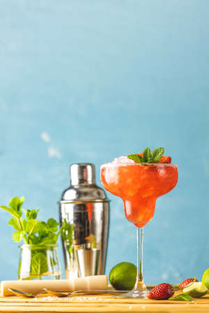 Frozen strawberry lime mint margarita in tall footed glass close up on the wooden table with bar tools and ingredients. Luxury alcohol fresh drink.の写真素材
