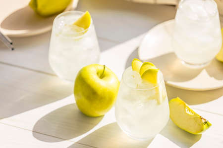 Summer cocktail with green apple and ice on the white table near window in the sunny summertime. Selective focus image with copy spaceの写真素材