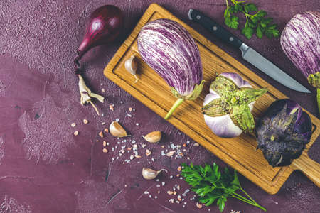 Different raw fresh eggplant on wooden cutting board. Concept of green house life style and products of subsistence farming, flat lay on claret concrete surface, copy spaceの写真素材