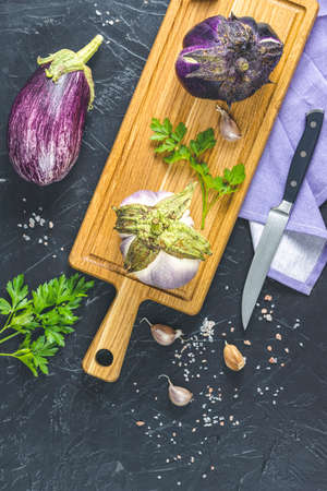 Raw fresh eggplant on wooden cutting board. Concept of green house life style and products of subsistence farming, flat lay on black concrete surface, copy space.の写真素材
