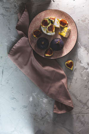 Blue or bleu cheese with fig and honey or maple syrup on pink plate. Artistic painting sunny light. Tasty white cheese flat lay top view.の写真素材