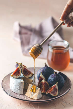 Sweet honey dripping from blue or bleu cheese with fig and honey or maple syrup on pink plate. Tasty white cheese close up view.の写真素材