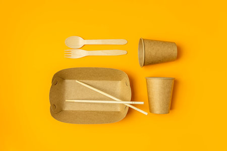 No more plastic. Bamboo cutlery and paper dishes on yellow background, flat lay. Zero waste concept.