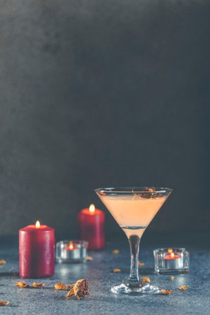 Summer grapefruit martini cocktail with dried roses flowers and petals, surrounded candles on dark gray table surface.の写真素材