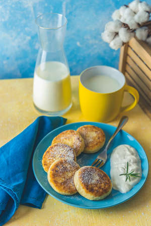 Cottage cheese pancakes, syrniki, ricotta fritters on ceramic plate. Gourmet healthy delicious morning breakfast. Copy space. Yellow and blue background.の写真素材