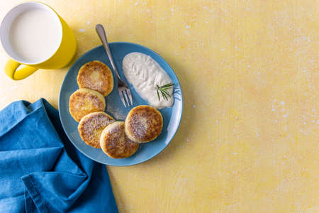 Cottage cheese pancakes, syrniki, ricotta fritters on ceramic plate. Gourmet healthy delicious morning breakfast. Top view, flat lay, yellow background.の写真素材