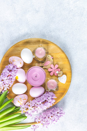 Easter greeting card with colored pink eggs and candles in wooden plate near hyacinths over light...