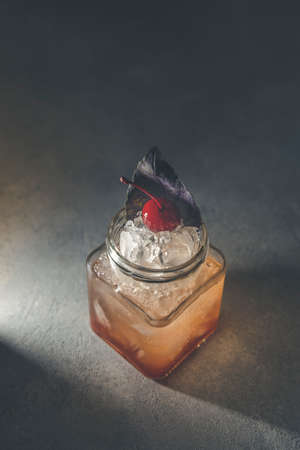 Picnic smash. Refreshing cold summer cocktail with grapefruit and  garnish by violet red basil leaves and cherry. Served in glass jar with crashed ice. Atmosphere of romantic date. Gray table surfaceの写真素材