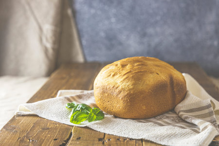 Loaf of freshly baked bread with basil on linen towel over rustic wooden table background. Selective...
