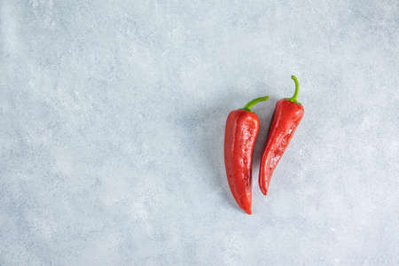 Fresh raw sweet red pepper kapi with water drops on light gray stone background, two peppers on gray table surface.の写真素材