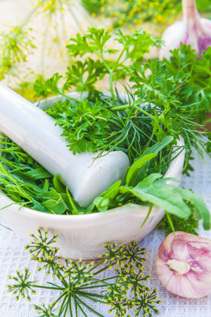 Mortar and pestle with fresh green herbs spices. Fresh dill, parsley, arugula in the pestle and garlic on the table. Herbs and spices on wooden board and white towel.の写真素材