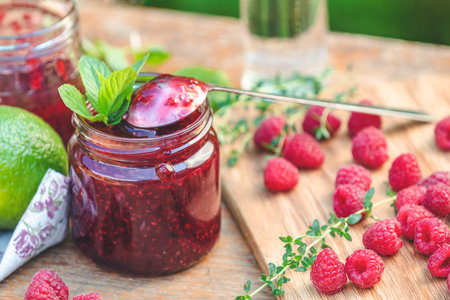 Raspberry jam and fresh raspberry on a rustic wooden table in the garden. Summer sunny day, close...
