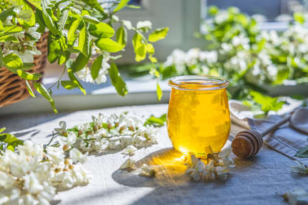 Sweet honey jar surrounded spring acacia blossoms. Sunny light, shallow depth of the field.の写真素材