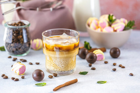Glass of brew cold coffee and ice. Cold summer drink on a light gray table surrounded coffee beans,...