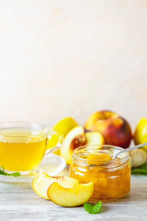 Fresh homemade peach jam in glass jar on a wooden background. Several fresh berries, lemon and mint...