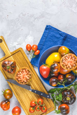 Slices raw fresh tomato. Colorful tomatoes and kitchen knife on wooden cutting board. Concept of green house life style and products of subsistence farming, flat lay on light gray concrete surfaceの写真素材