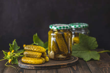 Fresh homemade pickled cucumbers in glass jar on a dark wooden background. Fresh cucumbers leaves are near it. Close up, selective focus.の写真素材