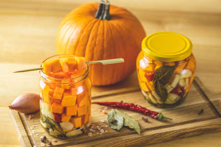 Fresh homemade pickled pumpkin in glass jar on a wooden background. Fresh pumpkin and spices are near it. Close up, selective focus.の写真素材
