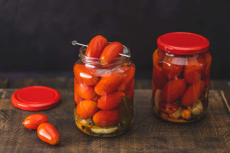 Pickled red cherry tomatoes in a glass jar on the old wooden background, selective focusの写真素材