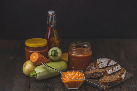 Squash zucchini paste or caviar and rye bread surrounded by the ingredients on dark wooden table....