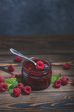 Homemade raspberry jam or marmalade in the glass jar and ripe raspberry on the wooden table
