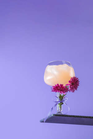 Glass of gin-tonic with slices of grapefruit decorated fresh chrysanthemums on bright violet background. Spring summer art drink food concept.の写真素材