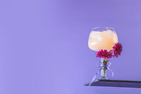 Glass of gin-tonic with slices of grapefruit decorated fresh chrysanthemums on bright violet background. Spring summer art drink food concept.の写真素材