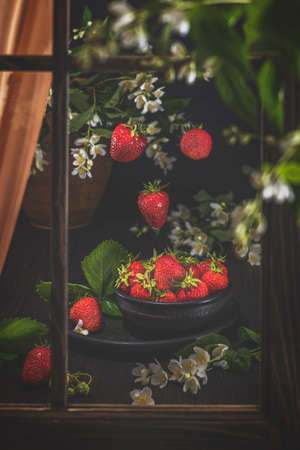 Fresh raw juicy strawberry in black ceramic  plate. Green leaves. Fresh mint. Dark wooden table. Shallow depth of field.の写真素材