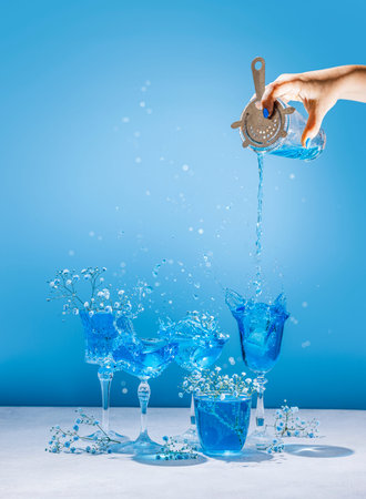 Different elegant champagne glasses with Blue Lagoon cocktail, women hand is pouring cocktail from...