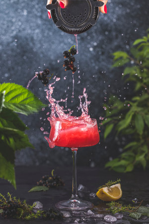 Elegant glass of Black Currant Gin Sour cocktail or mocktails with splash surrounded by ingredients on dark table surface. Refreshing drink ready for drinking.の写真素材