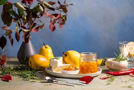 Pear jam in jar surrounded by ingredients, cheese and herbs on white plate and table on light gray background.の写真素材