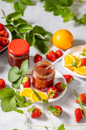 Strawberry jam in glass jars, accompanied by fresh strawberries and orange slices, creating a vibrant and appetizing sceneの写真素材