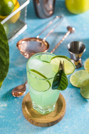 Refreshing green cocktail is being prepared with lime and ice on a bartop with bar tools