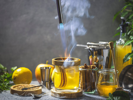 Glass with hot apple cocktail is getting heated by blowtorch in smoky bar setting with ingredients aroundの写真素材