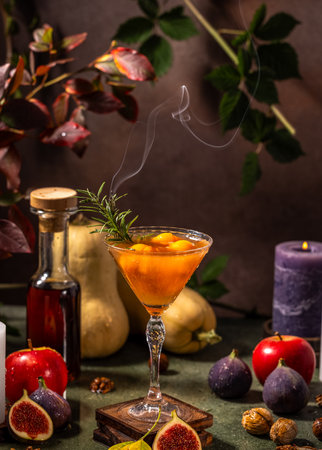 Smoking autumn cocktail is surrounded by figs, apples, butternut squash, walnuts, rosemary, and candles, creating a festive atmosphereの写真素材
